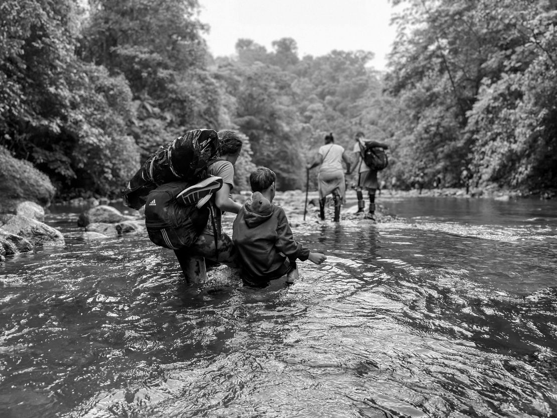 A Venezuelan woman guides her son through knee-high water, his dinosaur toy stuffed safely in his sweatshirt. She's hoping to get them to the US, to be reunited with her husband.