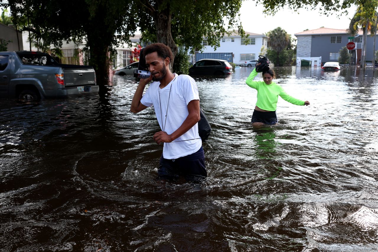 James Richard and Katherine Arroyo walk through a flooded street in Hollywood, Florida, on Thursday, April 13. The flooding came after the region experienced a 1-in-1,000 year rainfall event.