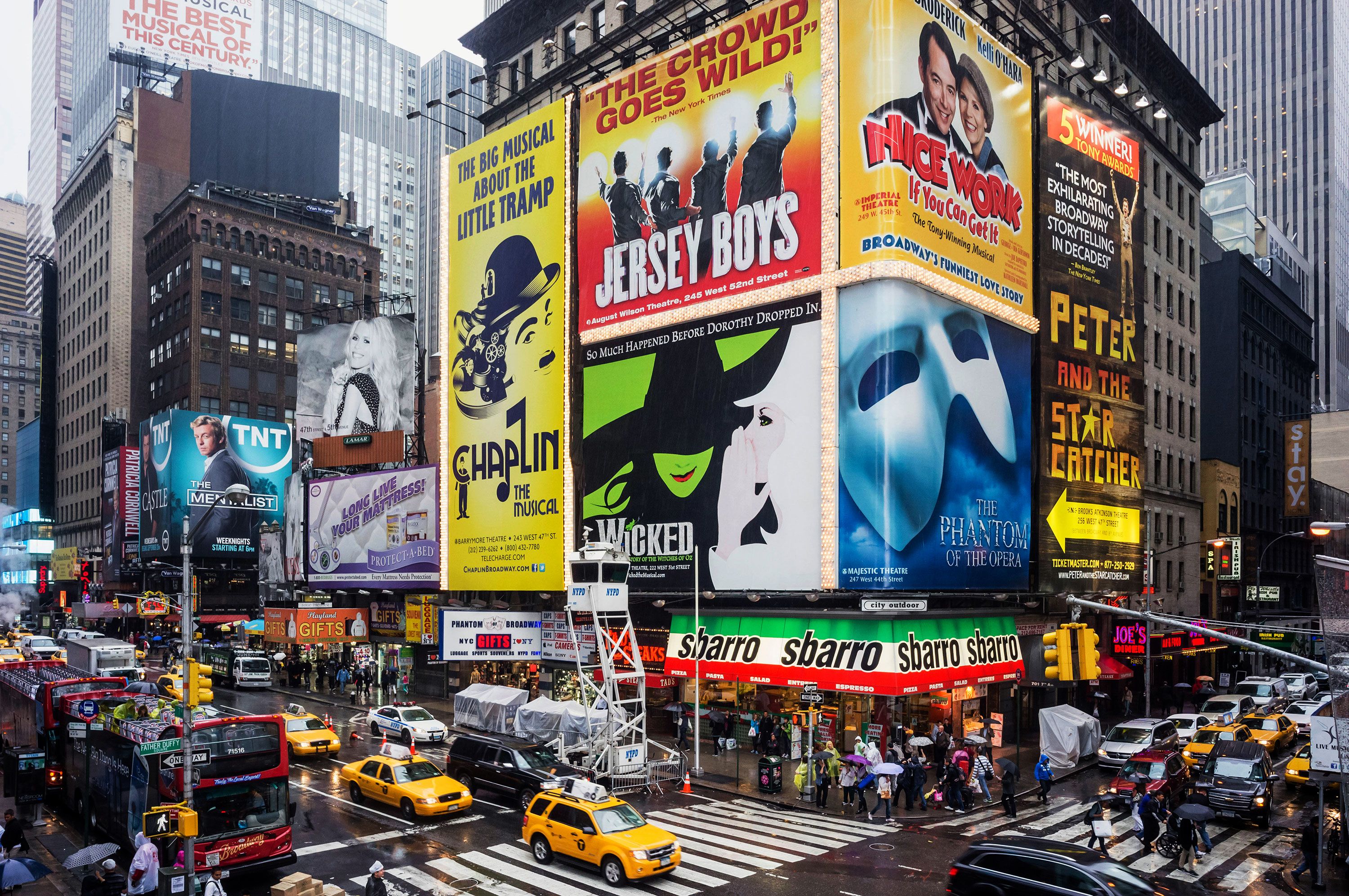 Broadway advertisements for 'Phantom' and other shows plaster a New York street corner.