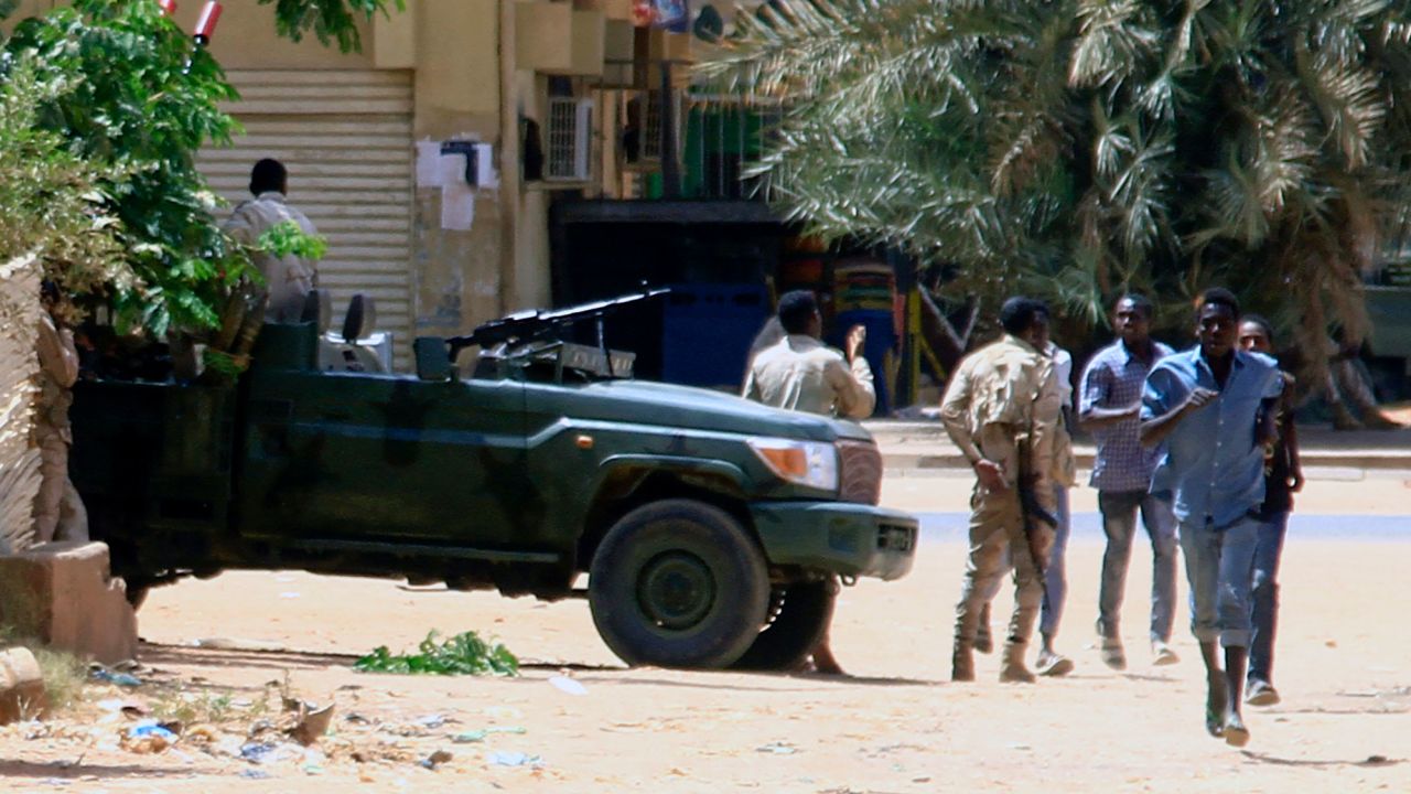 2023 年 4 月 15 日，人们在喀土穆跑过一辆军车，据报道该市发生冲突。 - 苏丹准军事组织表示，在 4 月 15 日与正规军发生战斗后，他们控制了几个关键地点，包括喀土穆市中心的总统府。 （照片由法新社提供）（照片由-/法新社通过盖蒂图片社提供）