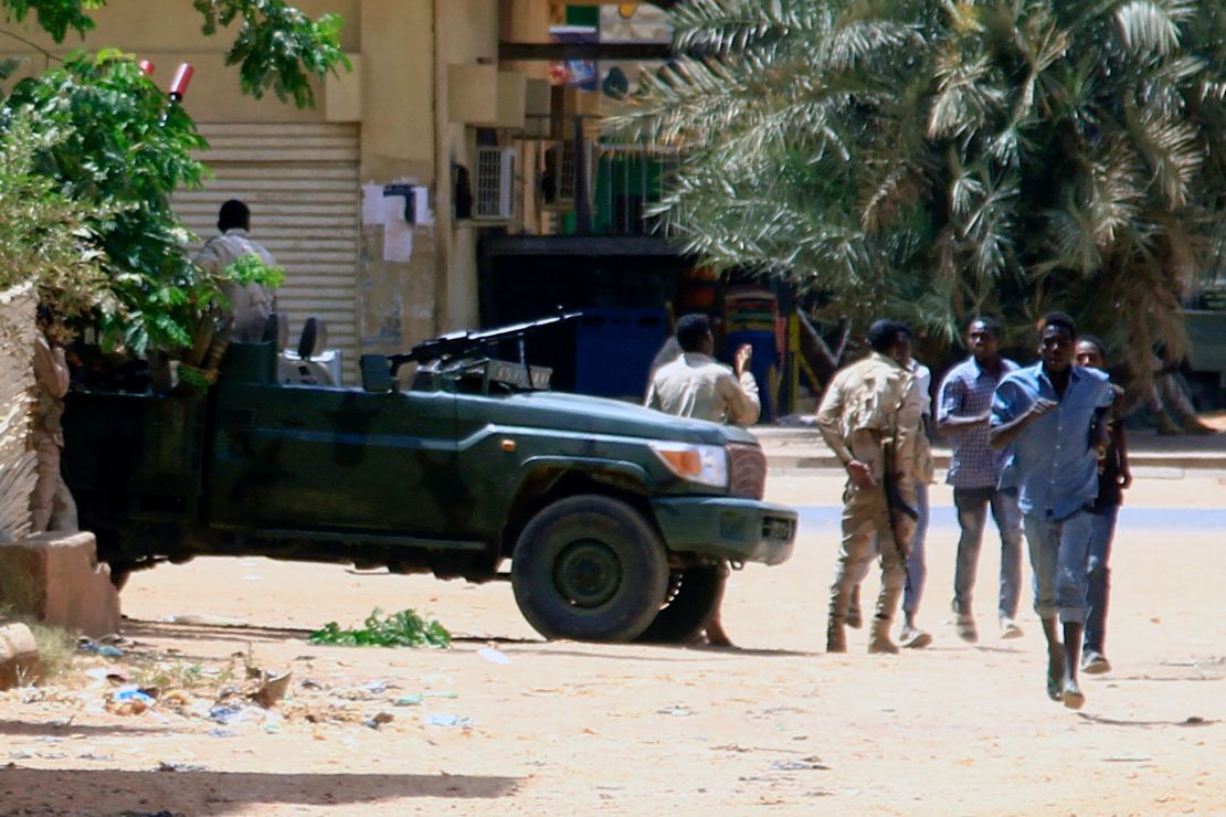 People run past a military vehicle in Khartoum on April 15, 2023, amid reported clashes in the city. - Sudan's paramilitaries said they were in control of several key sites following fighting with the regular army on April 15, including the presidential palace in central Khartoum. (Photo by AFP) (Photo by -/AFP via Getty Images)