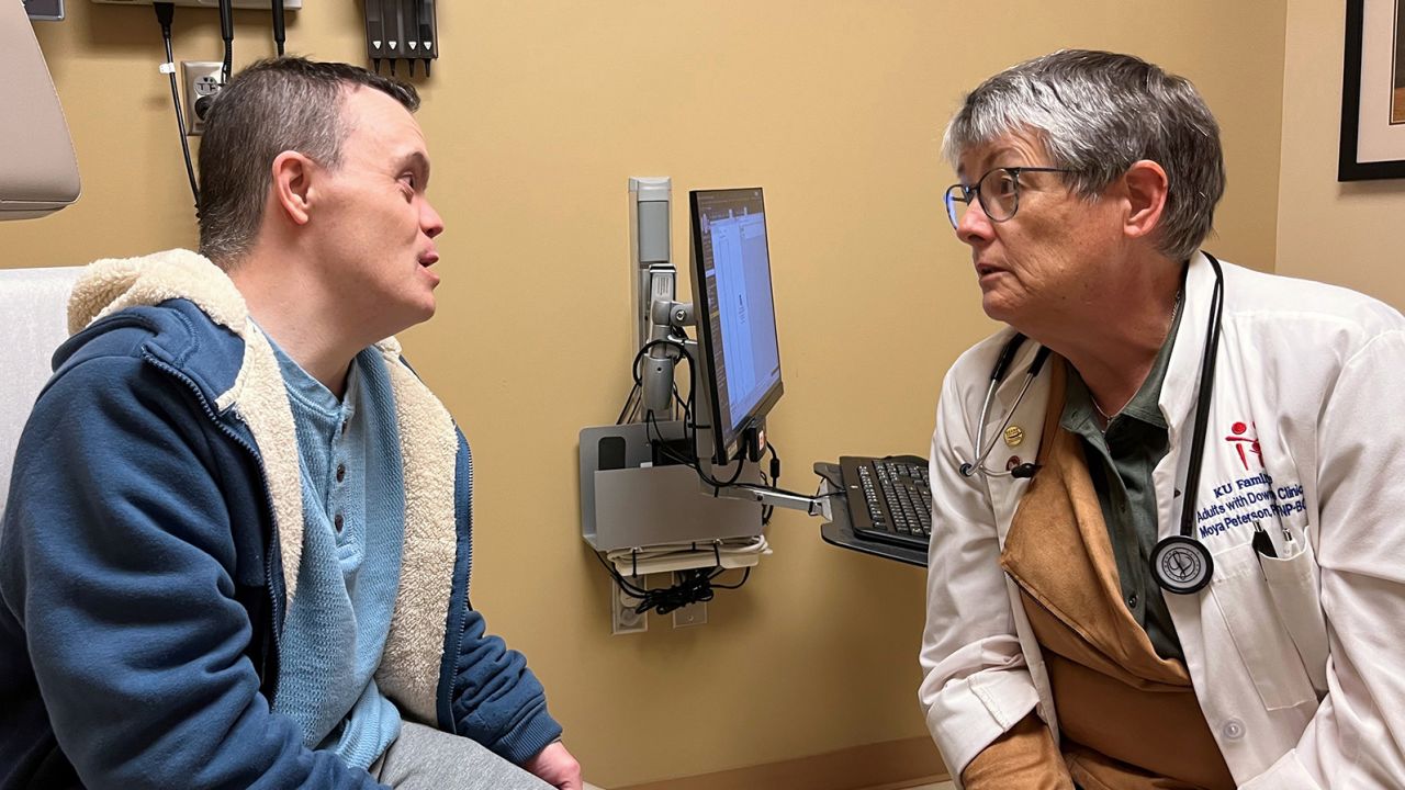 Pengamal jururawat Moya Peterson bercakap dengan Christopher Yeo dari Hartford, Kansas.  Peterson mengetuai klinik yang jarang ditemui untuk orang dewasa dengan sindrom Down. 