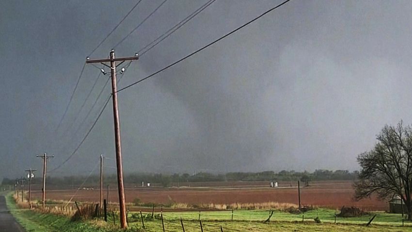 In this image taken from video, a massive funnel-shaped storm cloud makes its way over a road, as seen from a car, in Cole, Okla., Wednesday night, April 19, 2023. Strong storms, including tornadoes, winds and hail moved through parts of the Central U.S. on Wednesday, causing fatalities and injuries, destroying homes and leaving thousands without power.  (KOCO-TV via AP)