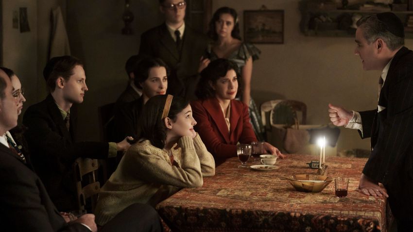 Jan and Miep Gies (Joe Cole and Bel Powley) join the Franks and the van Pels (from left: Liev Schreiber as Otto Frank, Ashley Brooke as Margot Frank, Rudi Goodman as Peter van Pels, Amira Casar as Edith Frank, Billie Boullet as Anne Frank and Caroline Catz as Mrs. van Pels) and watch as Mr. van Pels (Andy Nyman) lights the menorah during Hanukkah, as seen the upcoming limited series A SMALL LIGHT, from National Geographic and ABC Signature in partnership with Keshet Studios. (Photo credit: National Geographic for Disney/Dusan Martincek)