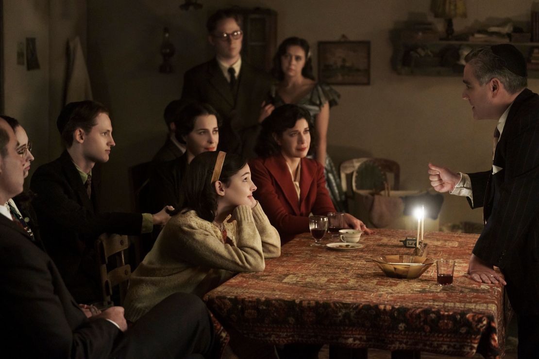 Jan and Miep Gies (Joe Cole and Bel Powley) join the Franks and the van Pels (from left: Liev Schreiber as Otto Frank, Ashley Brooke as Margot Frank, Rudi Goodman as Peter van Pels, Amira Casar as Edith Frank, Billie Boullet as Anne Frank and Caroline Catz as Mrs. van Pels) and watch as Mr. van Pels (Andy Nyman) lights the menorah during Hanukkah, as seen the upcoming limited series 'A Small Light.' 