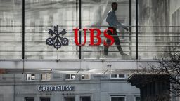 A employee is seen in silhouette with sign of Swiss giant banking UBS and a sign of Credit Suisse bank in Zurich on March 20, 2023. - Shares in European banks sank on March 20, 2022 despite a buyout of Credit Suisse by Swiss lender UBS aimed at preventing a global banking crisis. (Photo by Fabrice COFFRINI / AFP) (Photo by FABRICE COFFRINI/AFP via Getty Images)