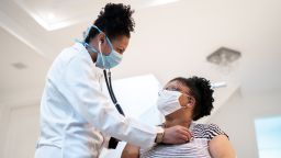 Doctor listening to patient's heartbeat during home visit - wearing face mask