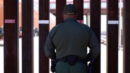 A US Customs and Border protection agent looks through the border fence as hundreds of migrants line up under the Stanton Street Bridge to be processed after illegally entering the US, in El Paso, Texas, on December 22, 2022. (Photo by Allison Dinner / AFP) (Photo by ALLISON DINNER/AFP via Getty Images)