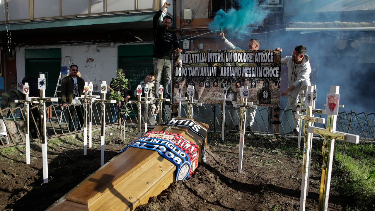 Supporters burn flares next to a mock grave for a coffin in Naples adorned with the scarves of rival teams Inter Milan, Juventus and AC Milan.