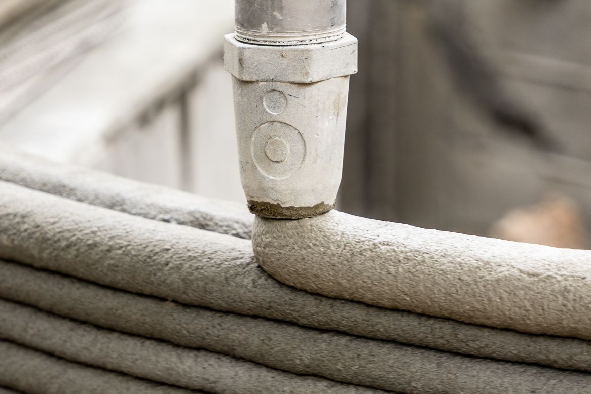 In 3D-printed construction, a cement mix is extruded from a nozzle to form layers that create vertical walls.