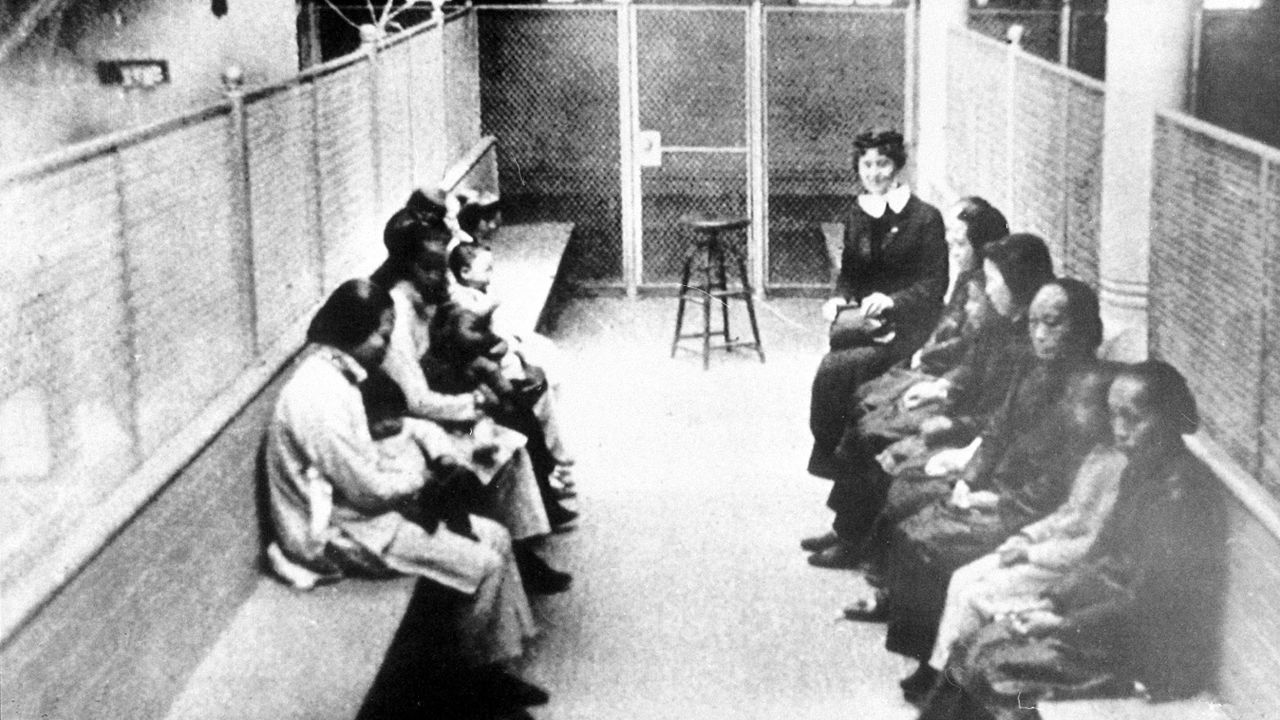 In this file photo from the 1920s, a group of Chinese and Japanese women and children wait to be processed as they are held in a wire mesh enclosure at internment barracks in Angel Island, California. As a result of the Chinese Exclusion Act and subsequent restrictions, immigrants were detained for extended periods of time there and faced the possibility of deportation.