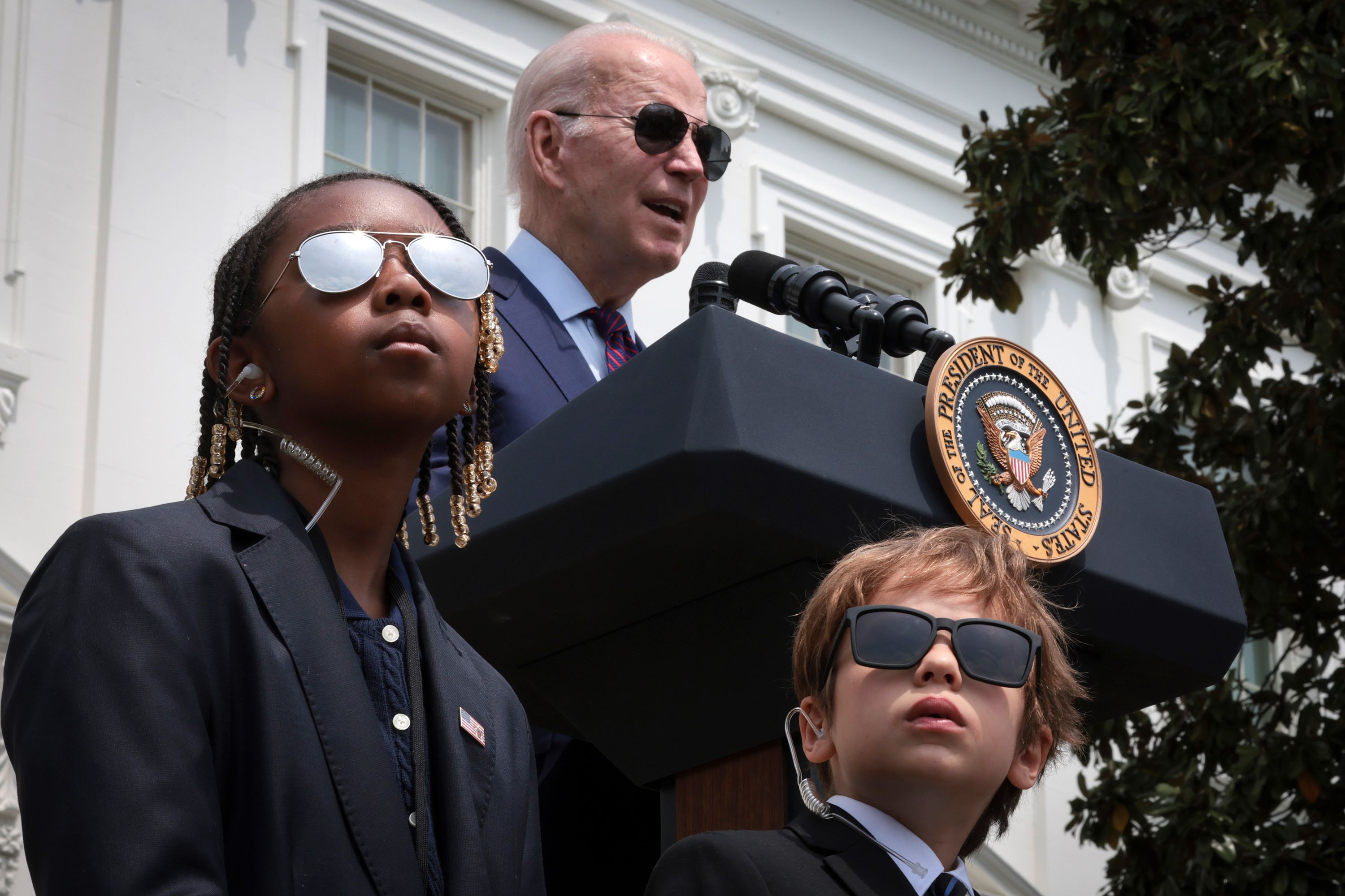 US President Joe Biden speaks while children dressed as Secret Service agents guard the stage.