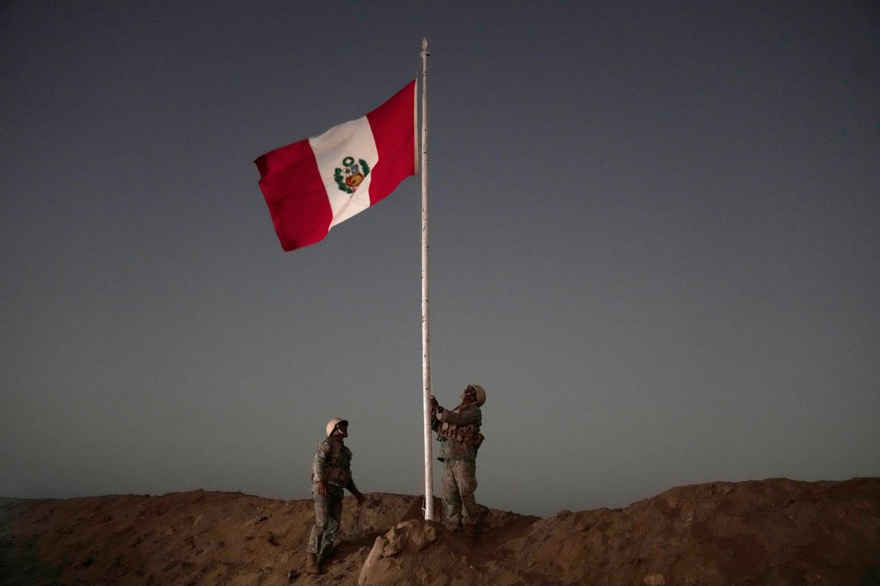 Peruvian soldiers raise their country's national flag in Tacna, Peru, near the border with Chile, on Friday, April 28. A migration crisis between Chile and Peru intensified the day before as hundreds of migrants remained stranded, unable to cross into Peru.