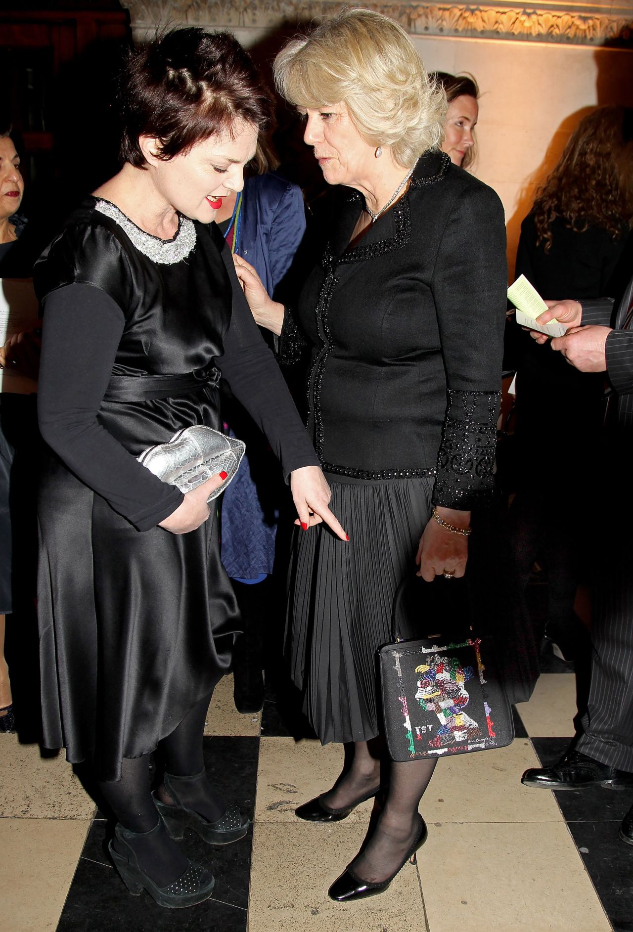 At the Royal Courts of Justice in 2010, Camilla met British designer Lulu Guinness. Guinness designed the black satin Jane bag worn by Camilla that evening. It featured a 1st Class stamp design embroidered in colorful sequins.