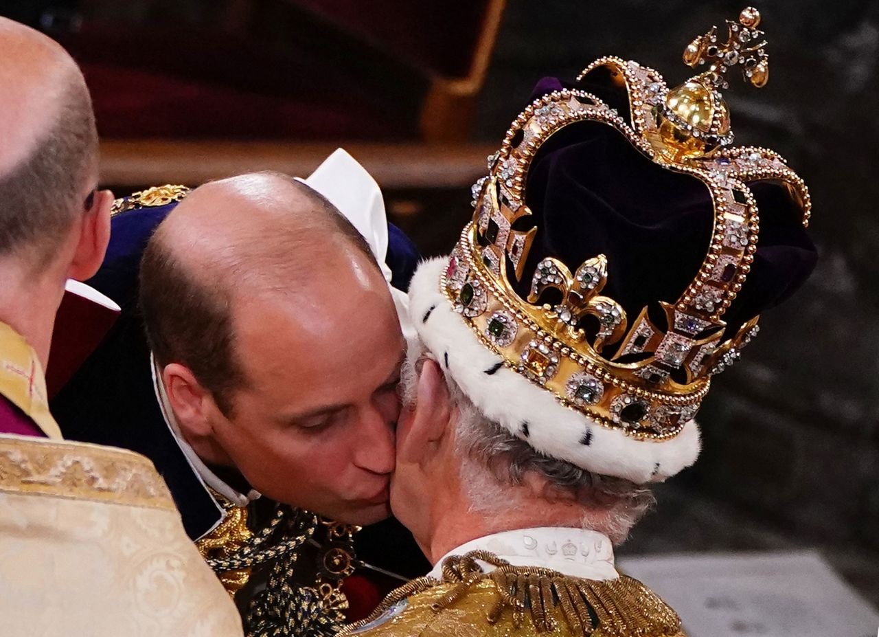 The King's son Prince William, the heir apparent to the throne, kisses his father on the cheek during the ceremony.
