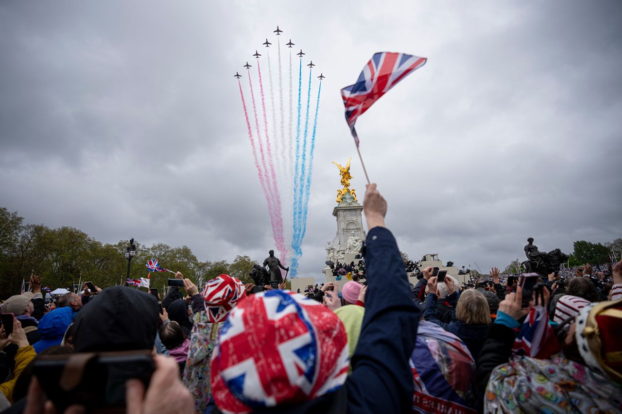 The Red Arrows, the aerobatics display team of the Royal Air Force, fly over Buckingham Palace as members of the public watch nearby. 