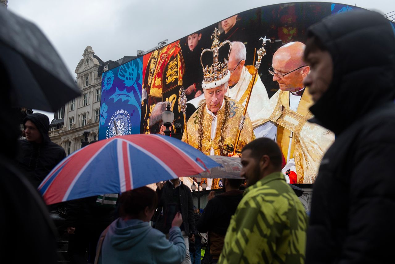 People in London's Piccadilly Circus walk past a giant screen showing an image of the King during the coronation ceremony.