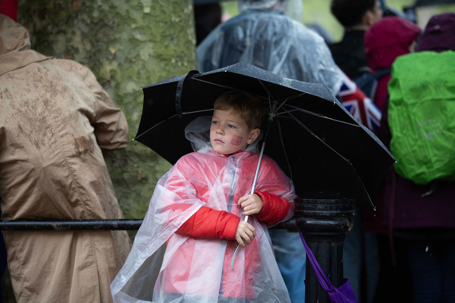 A boy holds an umbrella as he watches history unfold.