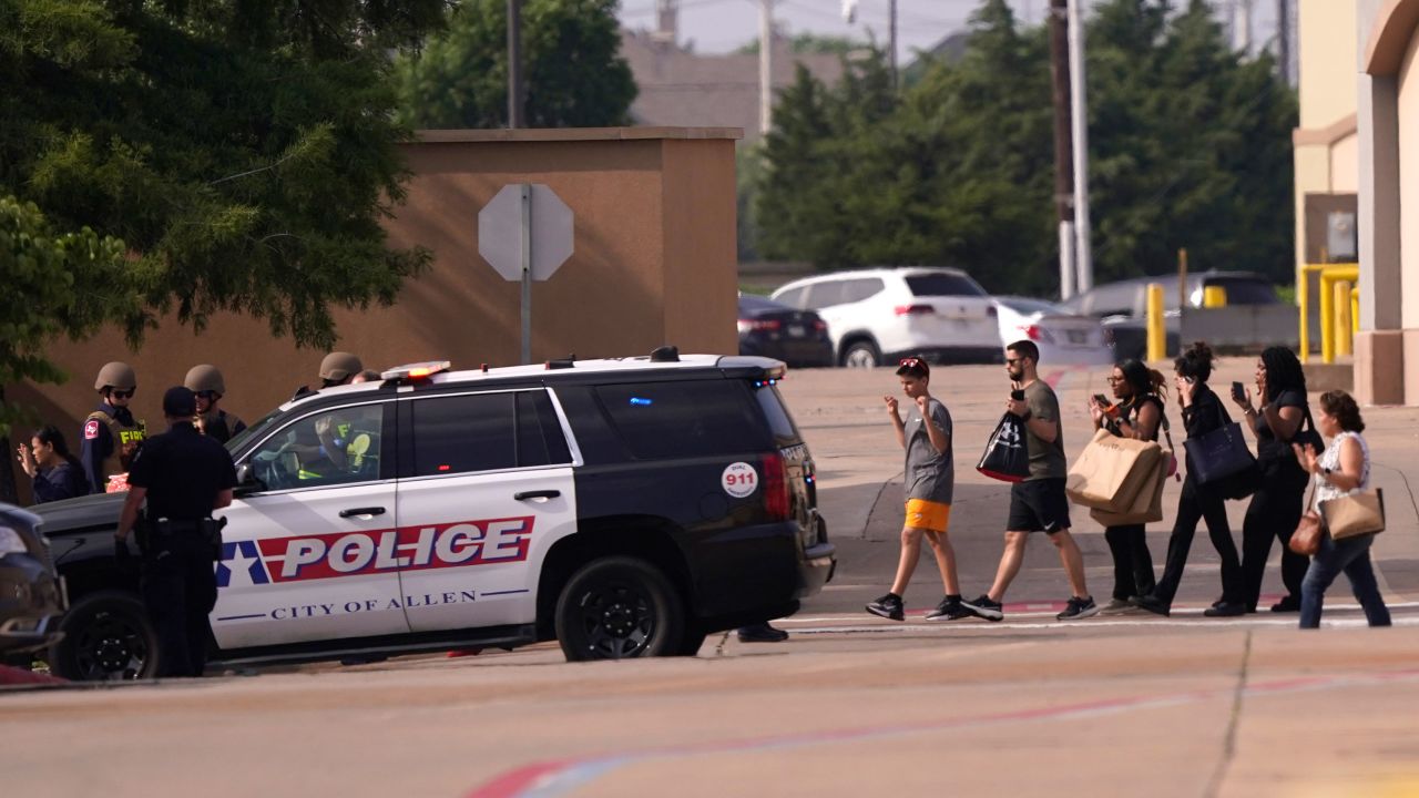 People raise their hands as they leave the Allen Premium Outlets after a shooting on May 6, 2023.