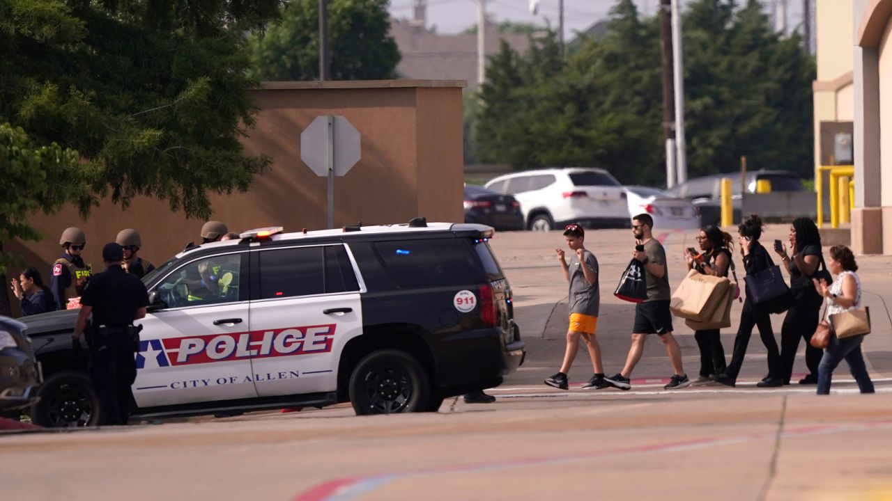 People raise their hands as they leave a shopping center after the shooting Saturday.