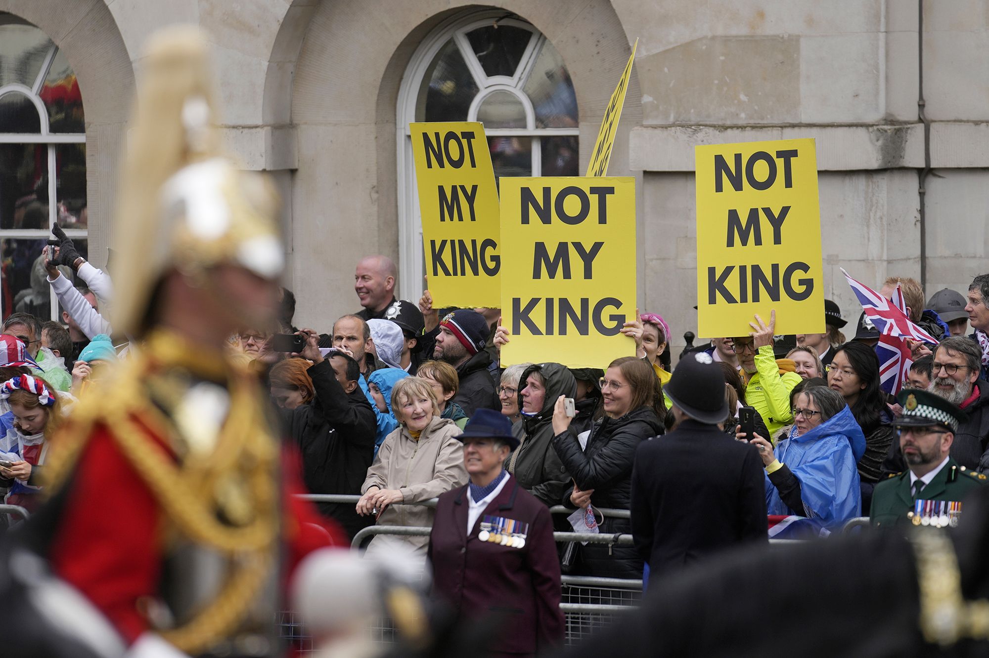 The procession passes anti-monarchy protesters.