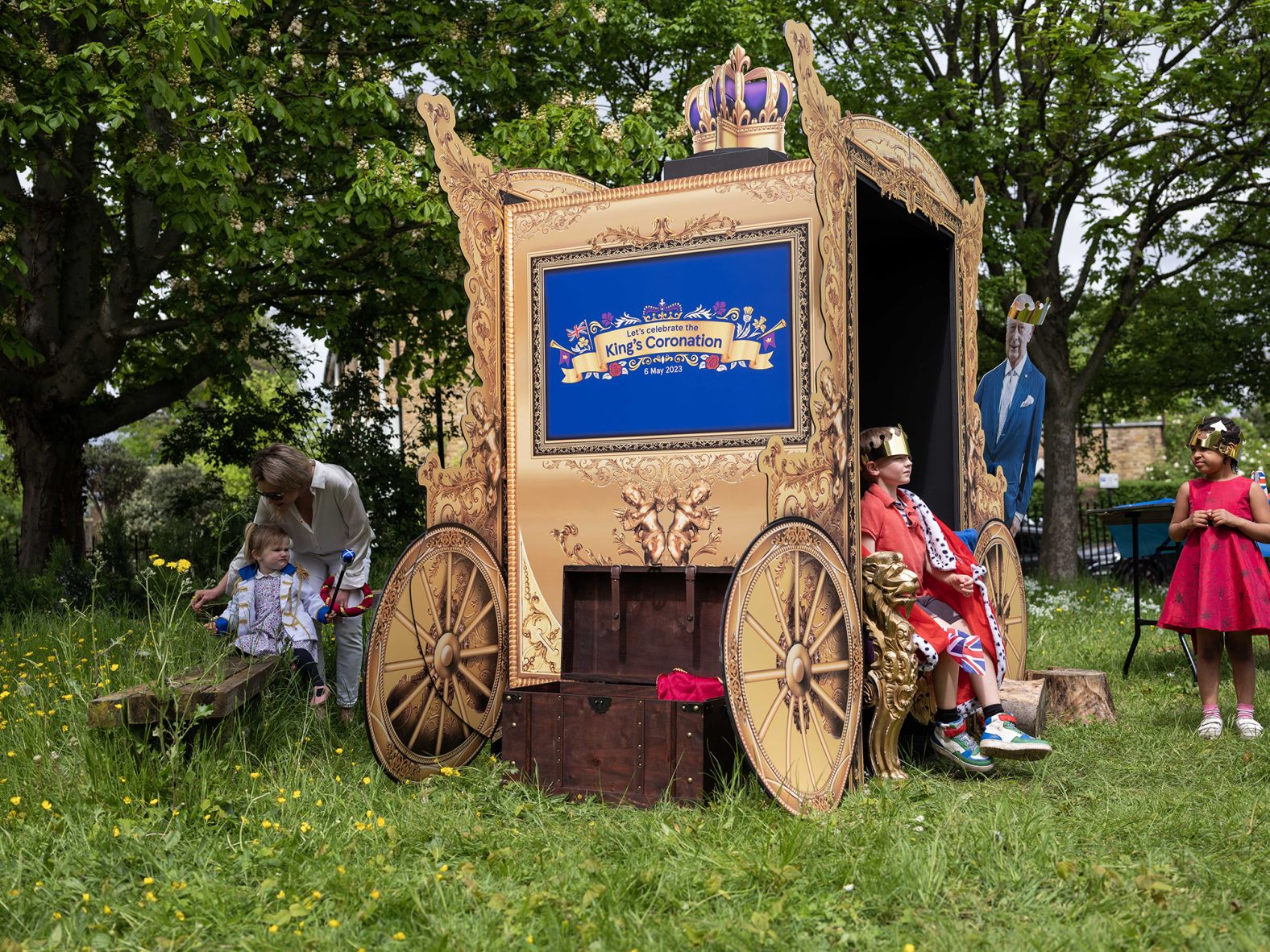 Kids play and pose for pictures at a makeshift carriage next to a cardboard cutout of the King at a street party in London.