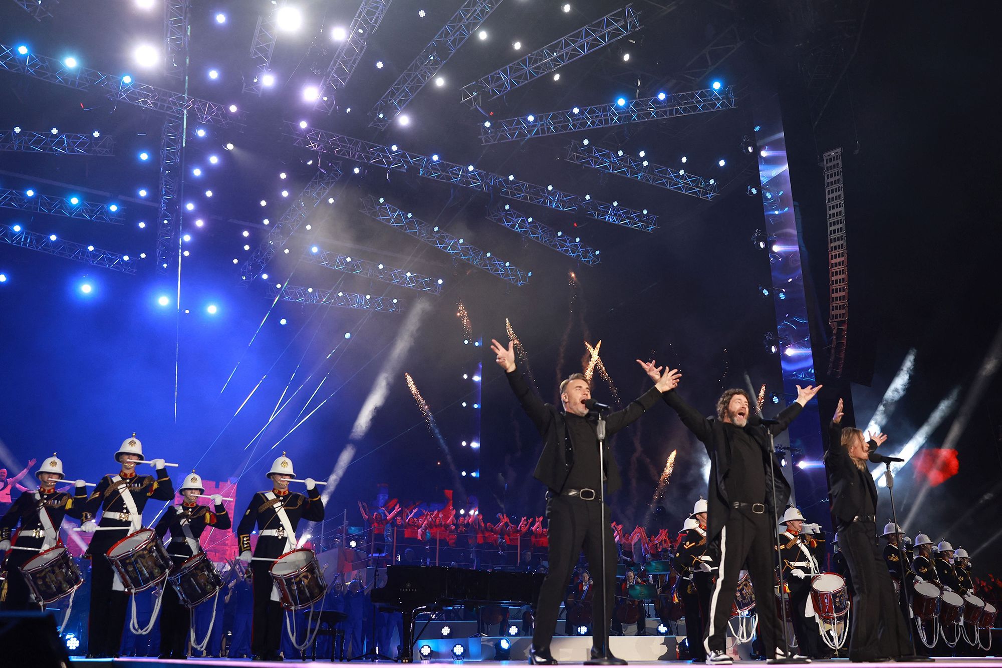 Gary Barlow, Howard Donald, and Mark Owen of '90s British pop group Take That perform backed by military drummers.