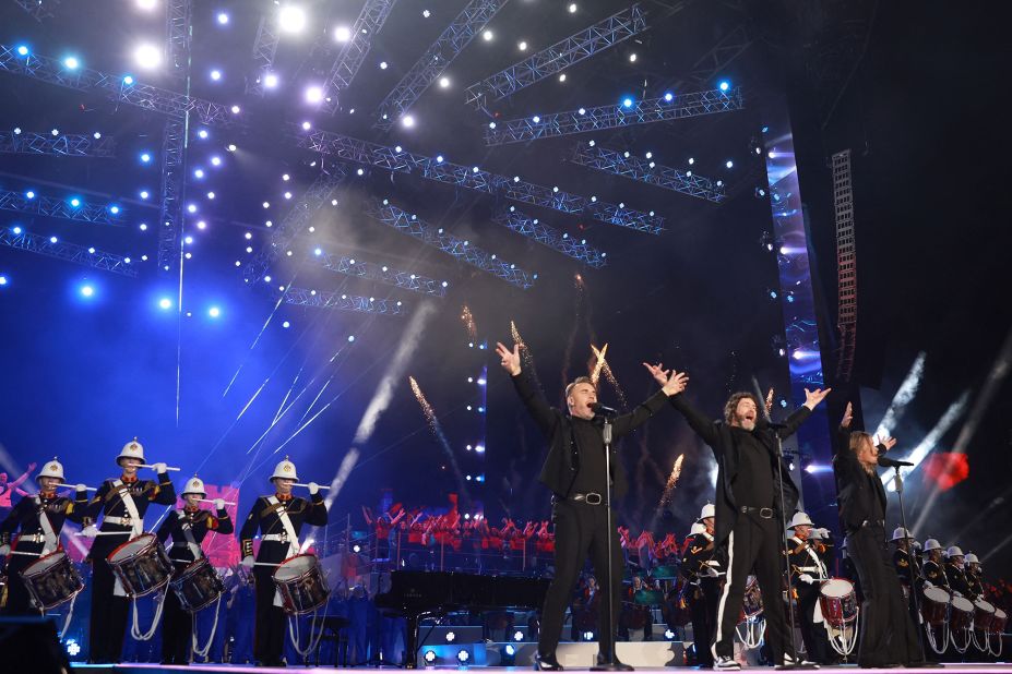 Gary Barlow, Howard Donald and Mark Owen of '90s British pop group Take That perform backed by military drummers.