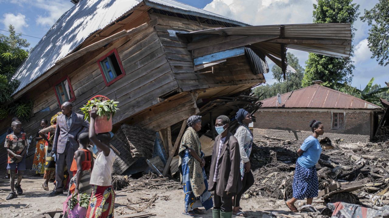 People walk next to a house destroyed by the floods in the village of Nyamukubi, South Kivu province, in Congo, Saturday, May 6, 2023.