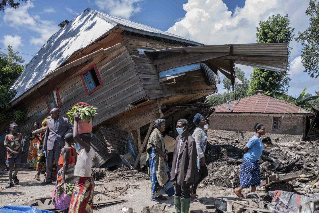 People walk next to a house destroyed by the floods in the village of Nyamukubi, South Kivu province, in Congo, Saturday, May 6, 2023.