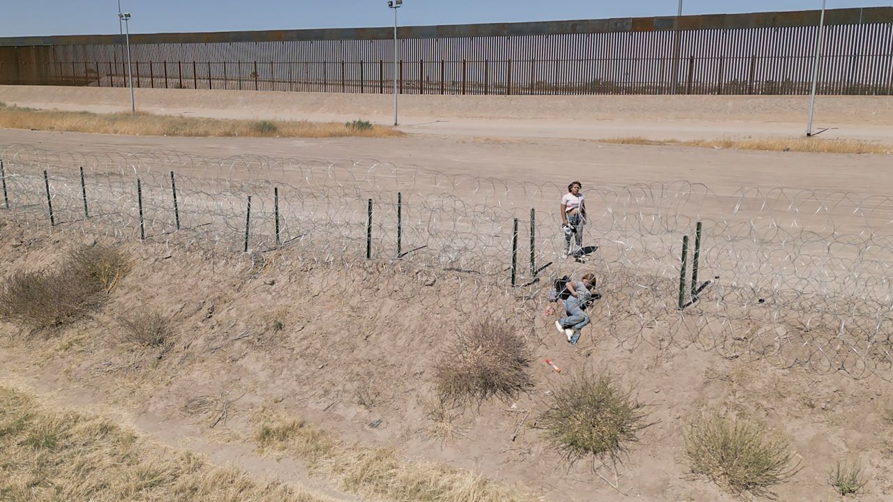 A woman helps a companion crawl through newly installed barbed wire at the US border.