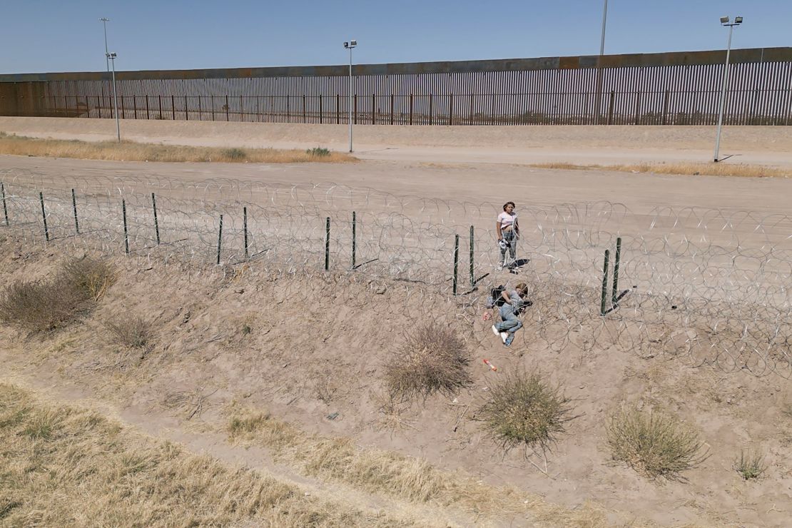 A woman helps a companion crawl through newly installed barbed wire at the US border.