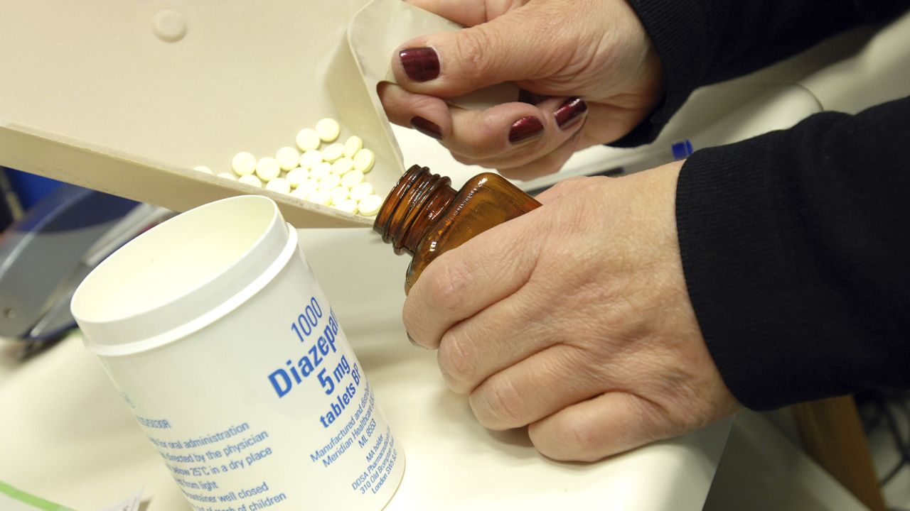 A pharmacist dispenses diazepam tablets, a controlled medication, into a pill bottle.