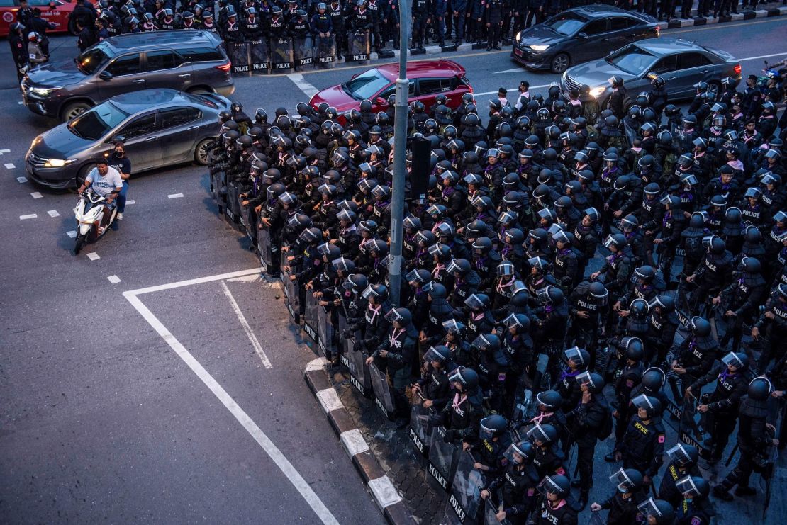 Motorists ride past riot police in Bangkok on October 15, 2020, after Thailand issued an emergency decree following an anti-government rally the previous day. 