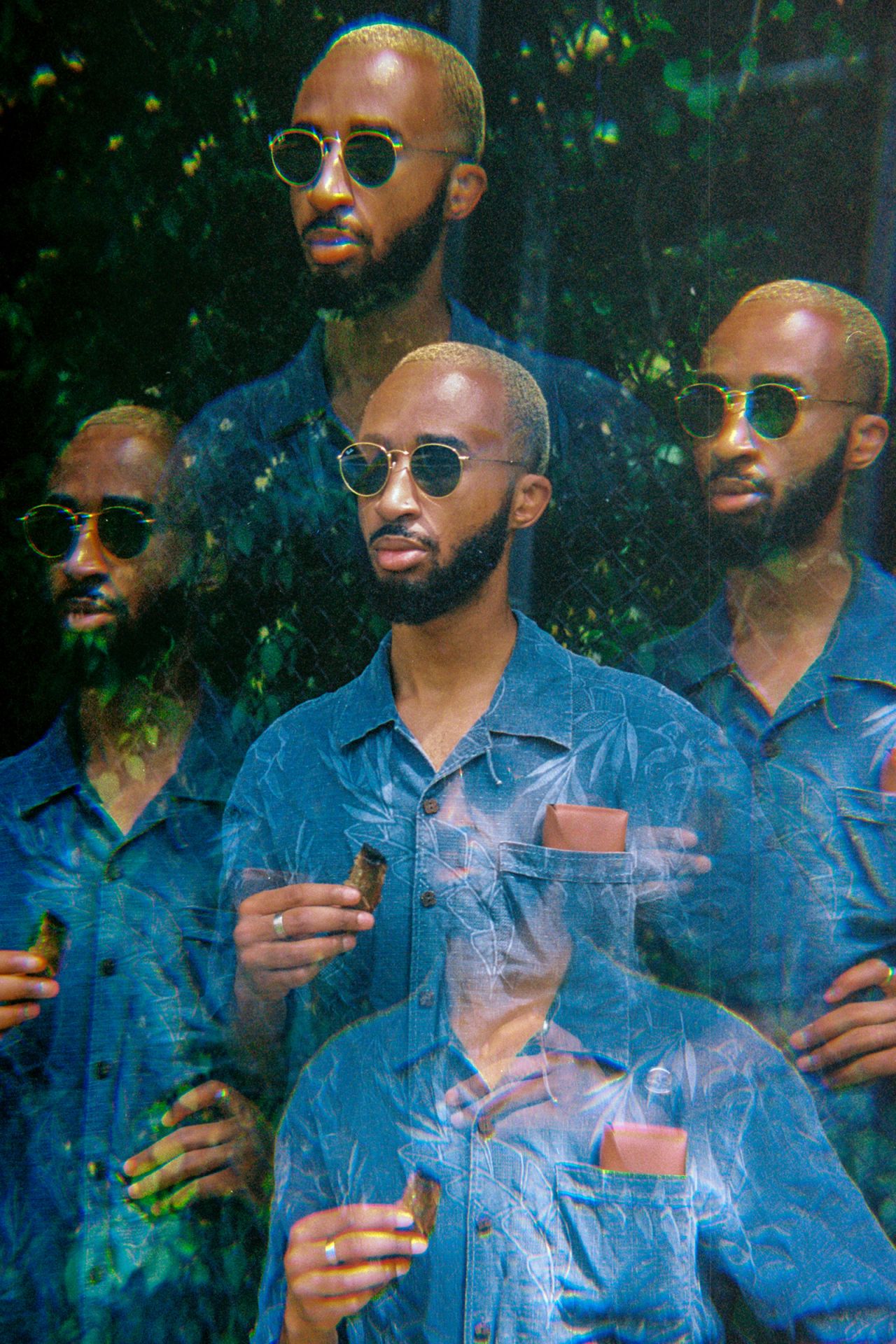 Ezemdi in sunglasses and a blue shirt, standing in the same position as his father's old photo.