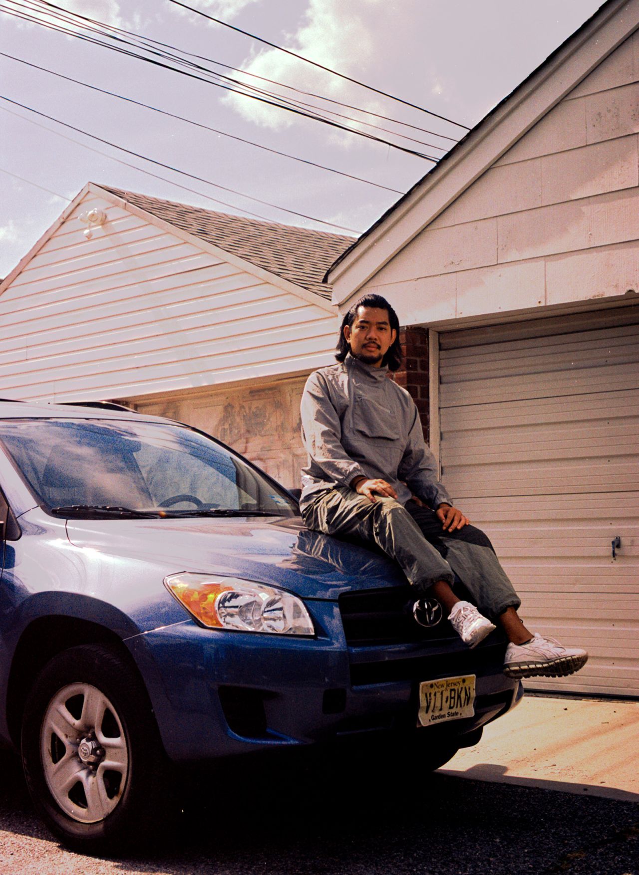 Tinhua sits on a blue car, mimicking his mother's pose in an old photo. The recreated images were shot on film, to match the intimate feel of the archival photos.