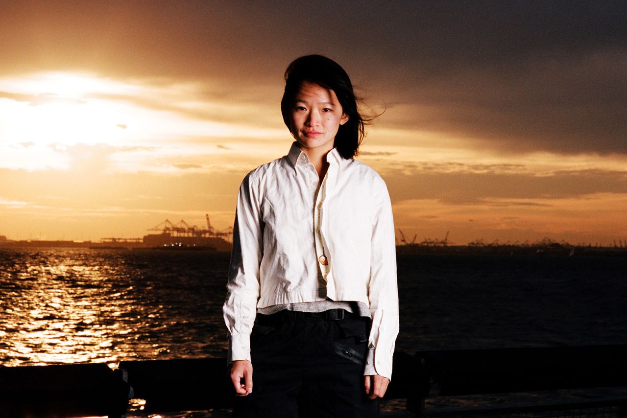 Julie, pictured by a waterfront. The photo series uses archival photos of immigrant parents to inspire similar shots of their children, who were born or raised in the United States.