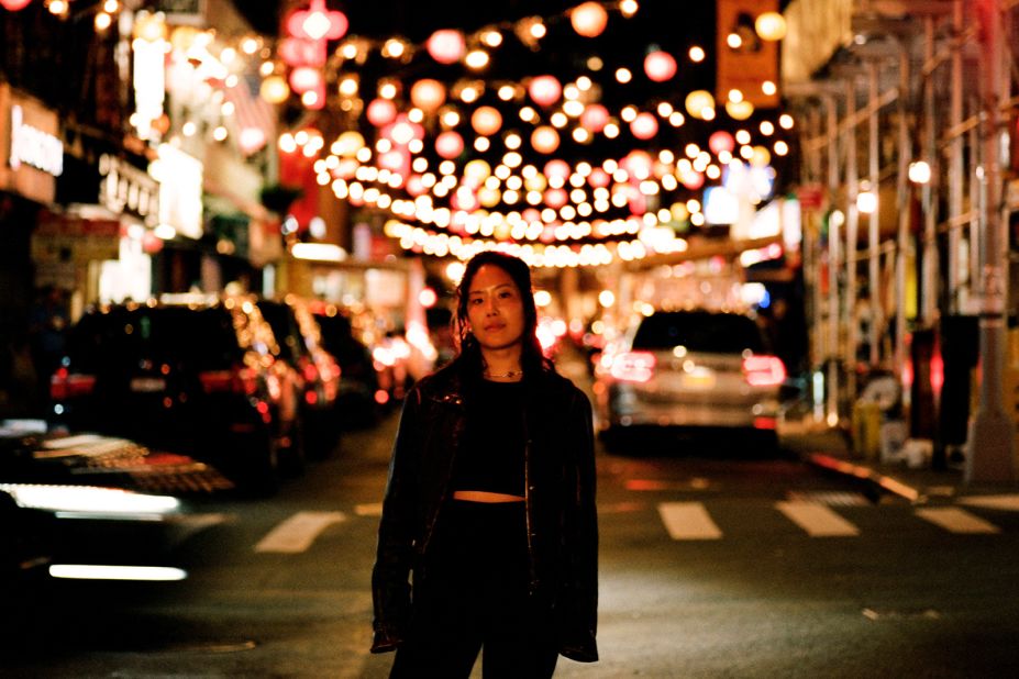 A young woman stands under string lights in New York City. 