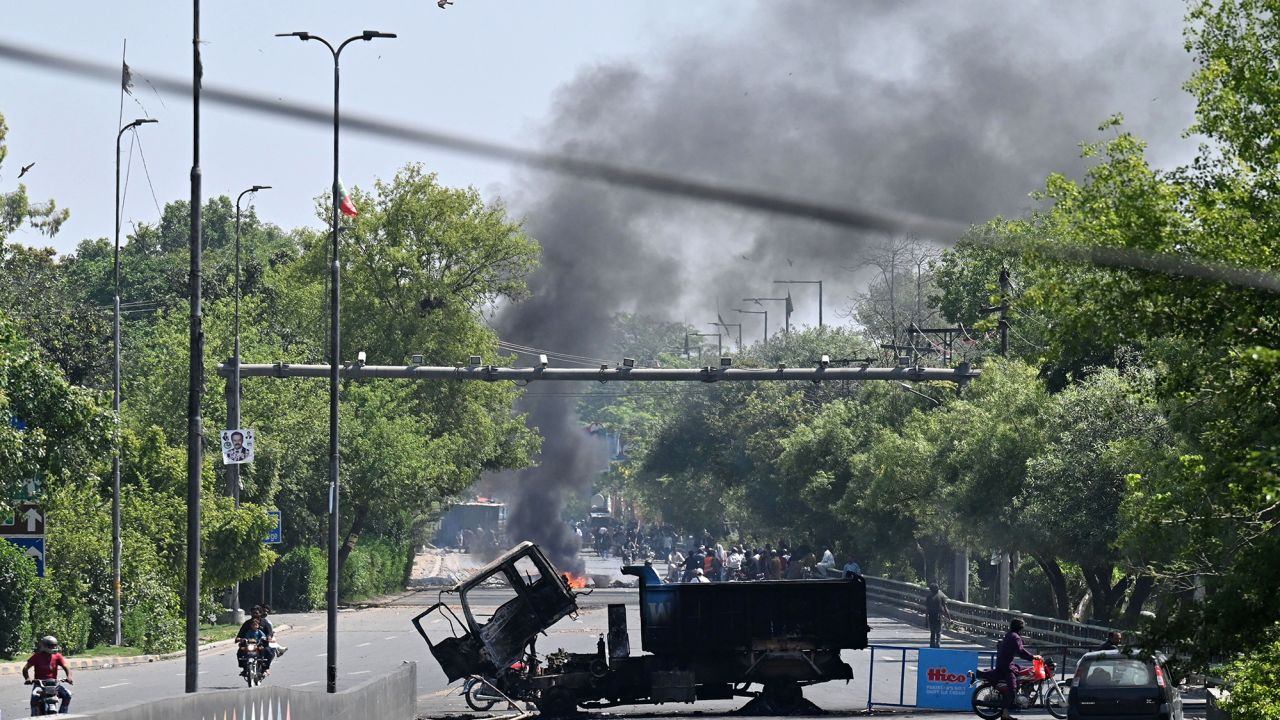 Motorists drive past burnt vehicles in front of Zaman Park in Lahore on May 10, 2023. 