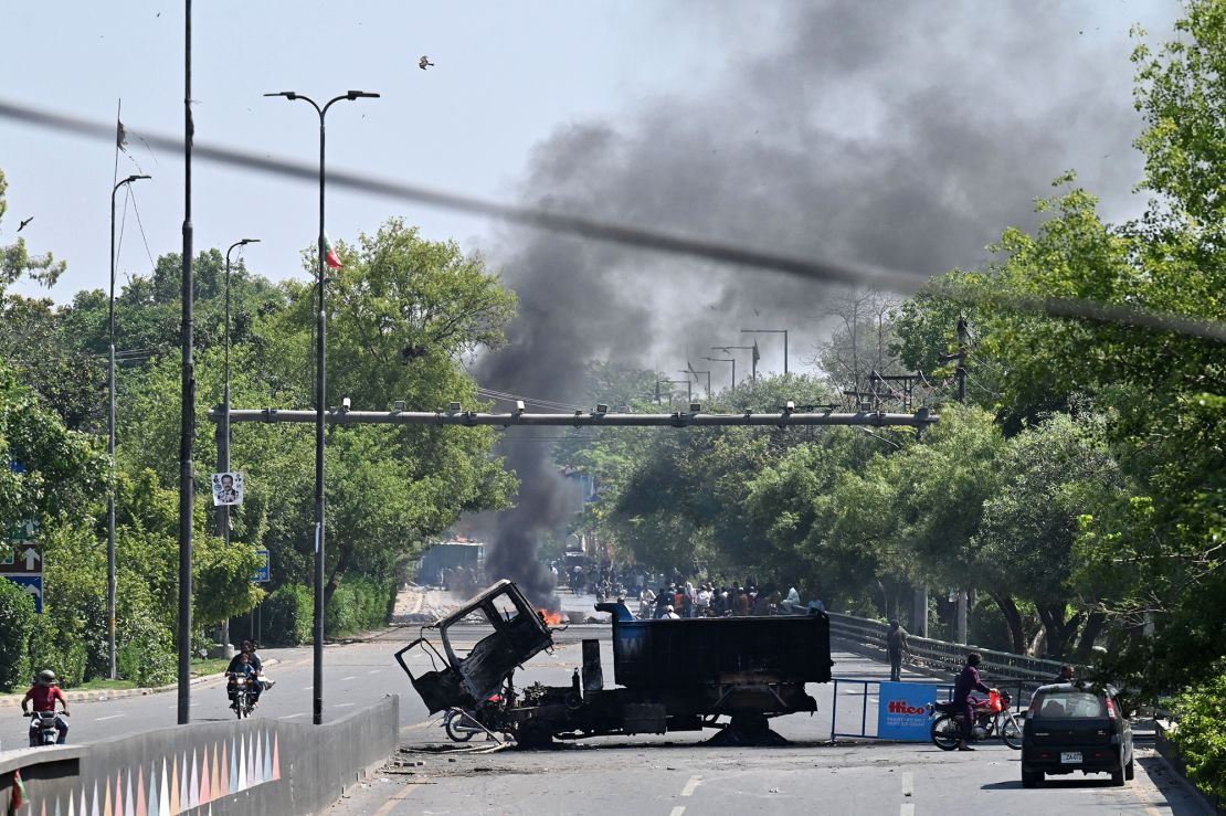 Motorists ride past burnt vehicles in front of the Zaman Park, a day after protests by Pakistan Tehreek-e-Insaf (PTI) party activists and supporters of former Prime Minister Imran Khan, in Lahore on May 10. 