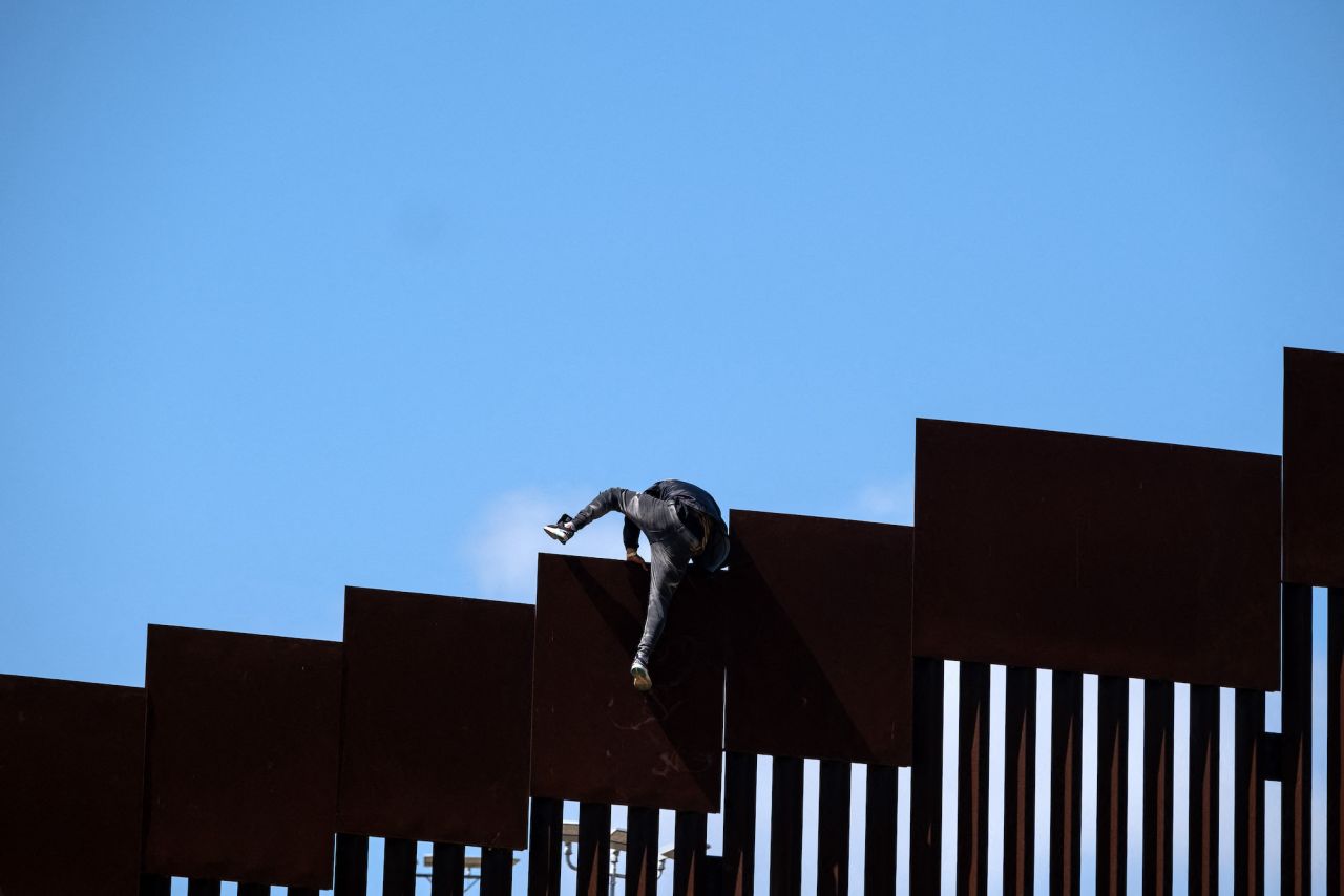 A migrant climbs over a border wall separating Tijuana, Mexico, from the United States after fetching groceries for other migrants who were waiting to be processed by US authorities on May 10.