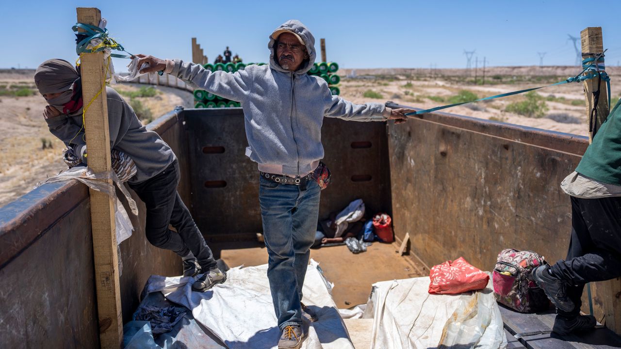 A man stands on top of carboard and makeshift bedding that the travelers place on top of the construction beam cargo to try to create some padding