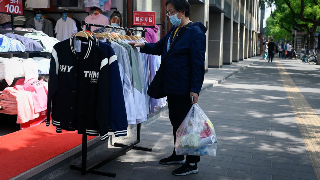 A customer browses through discount clothing displayed outside a shop in Beijing on May 10, 2023. 