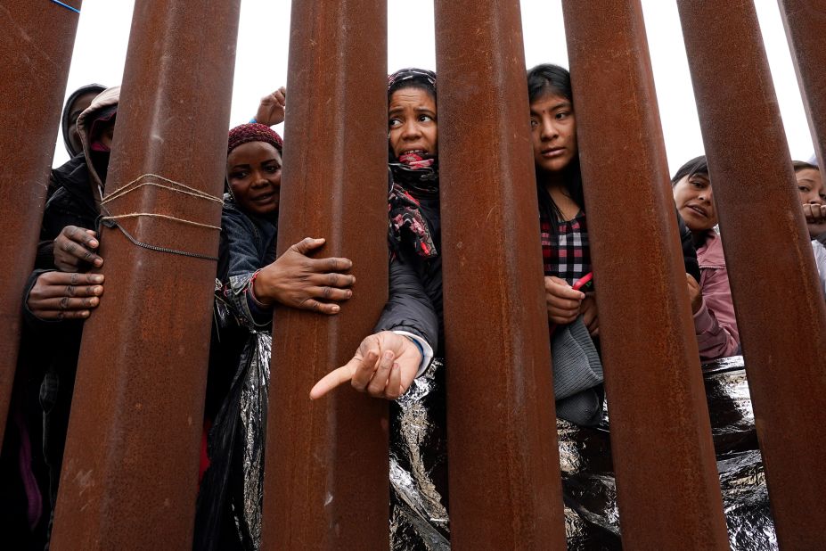 Migrants waiting to apply for asylum near San Diego reach through a border wall for clothing handed out by volunteers on May 12.