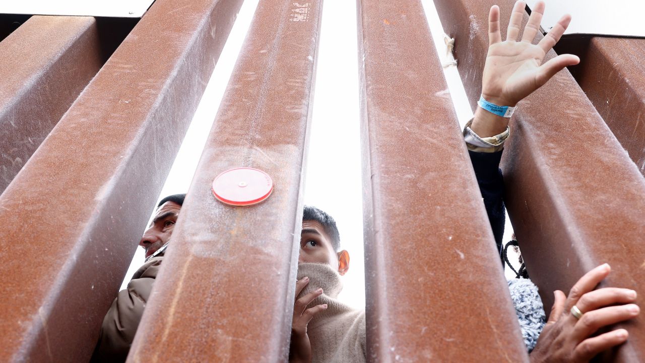 Migrants seeking asylum in the US look through the border wall as volunteers offer assistance on the other side on Saturday in San Diego.