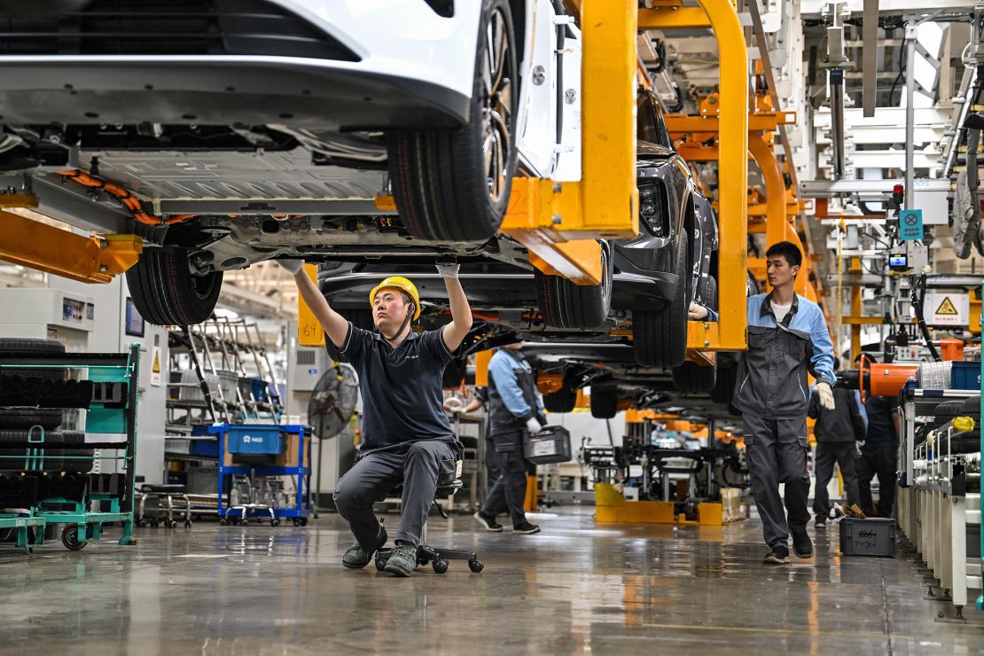 An employee (C) checks under a car along the assembly line at a factory of Chinese automaker NIO in Hefei, in China's eastern Anhui province on May 10, 2023. (Photo by Hector RETAMAL / AFP) (Photo by HECTOR RETAMAL/AFP via Getty Images)