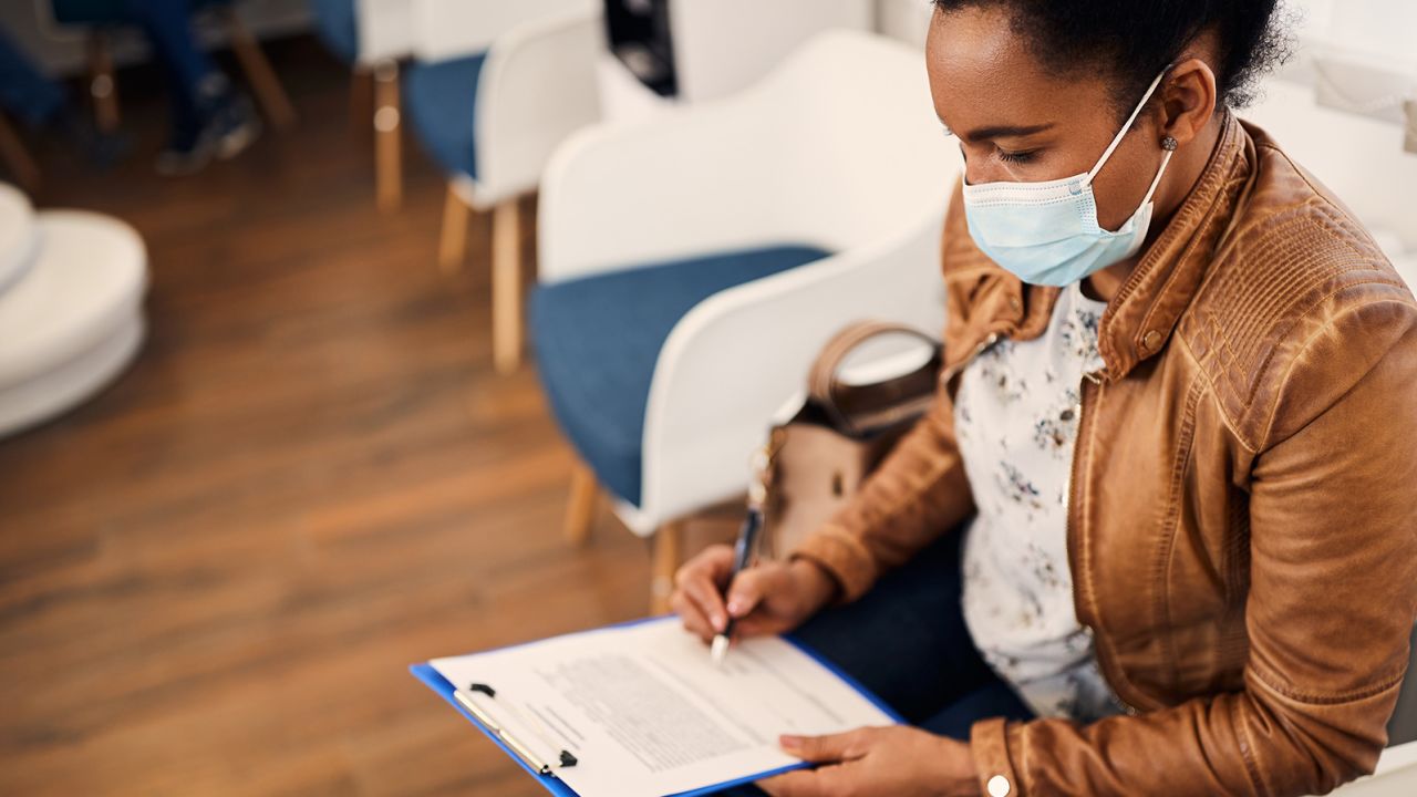 Black woman writing her data in medical document before dental examination. She is wearing protective face mask due to COVID-19 pandemic.