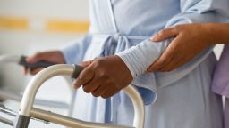 Nurse helping woman use walker in hospital hallway - stock photo