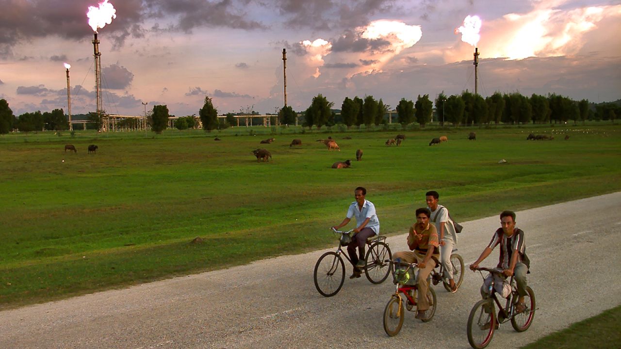 Acehnese men bicycle to work past an Exxon Mobil gas production facility in Lhokseumawe, Aceh province, Indonesia on April 4, 2001.