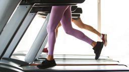 Low section of two attractive people running on treadmills in the gym.